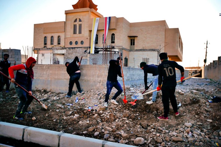 Pessoas consertam uma rua destruída durante confrontos contra militantes do Estado Islâmico em Qaraqosh, Iraque, em 23 de fevereiro.