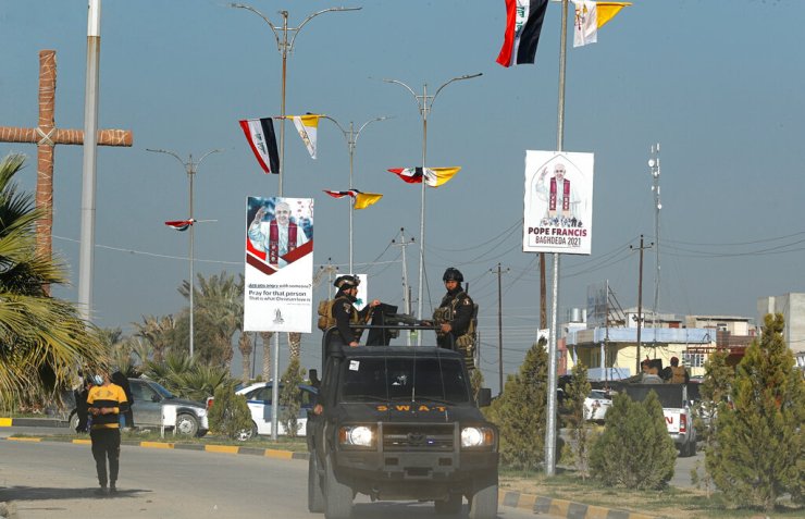 As forças de segurança iraquianas em Qaraqosh passam pelas bandeiras do Iraque e do Vaticano e cartazes anunciando a próxima visita do Papa Francisco em 22 de fevereiro.
